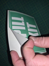Load image into Gallery viewer, Hand holding a green and white 'Spill Kit' sign on a grid background