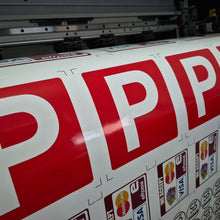 Load image into Gallery viewer, Large roll of paper with red 'P' letters and logos on a printing machine.