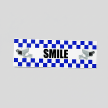Load image into Gallery viewer, Close-up of a commercial storefront entrance with a 'SMILE You're on Camera' STICKER prominently displayed.