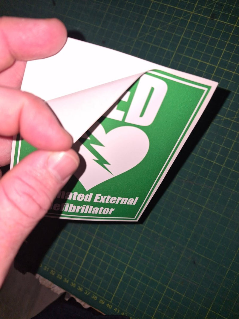 Hand holding a green and white card with an AED symbol on a grid background