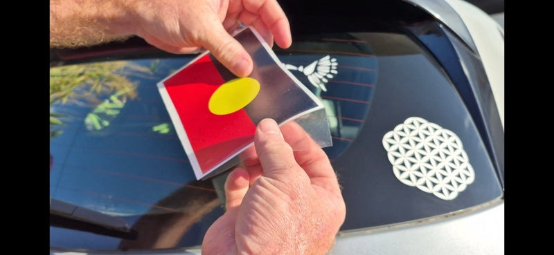 Person holding a car decal with a red and yellow design, applying it to a vehicle's window.