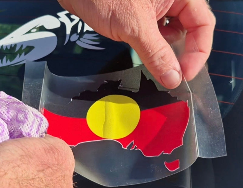 Hand holding a clear plastic sheet with an Aboriginal flag design.