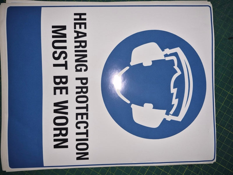 Sign with a helmet icon and text 'Hearing protection must be worn' on a white background with blue border.