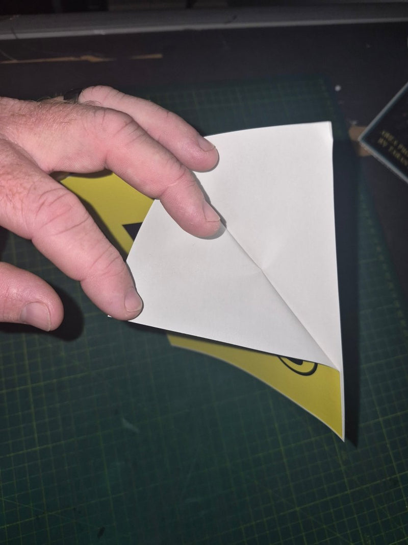 Hand holding a white paper l plate sticker on a green cutting mat