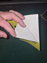 Load image into Gallery viewer, Hand holding a white paper l plate sticker on a green cutting mat
