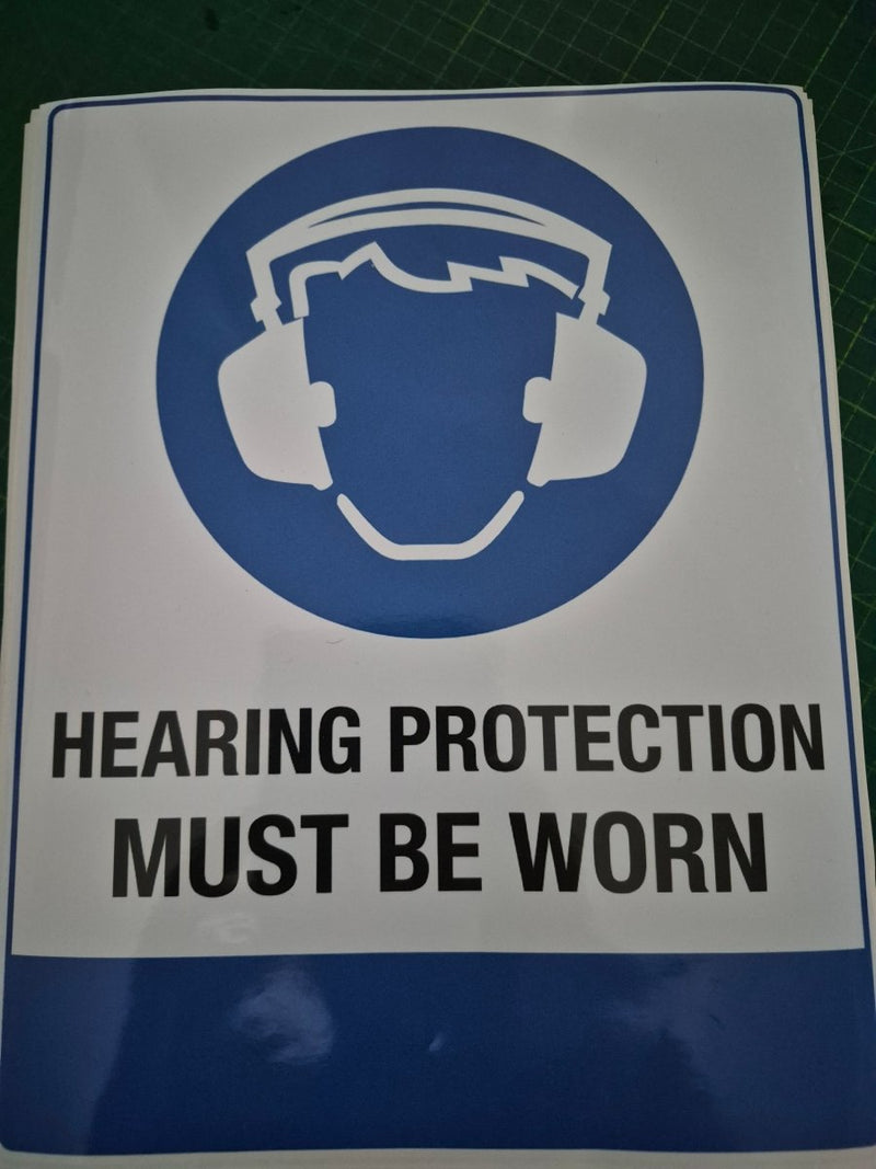 Sign with a hard hat icon and text 'Hearing protection must be worn' on a blue and white background.