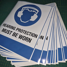 Load image into Gallery viewer, Stack of 'Hearing Protection Must Be Worn' signs on a green cutting mat.
