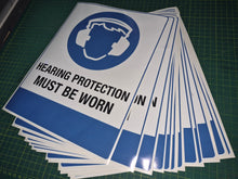 Load image into Gallery viewer, Stack of 'Hearing Protection Must Be Worn' signs on a green cutting mat.

