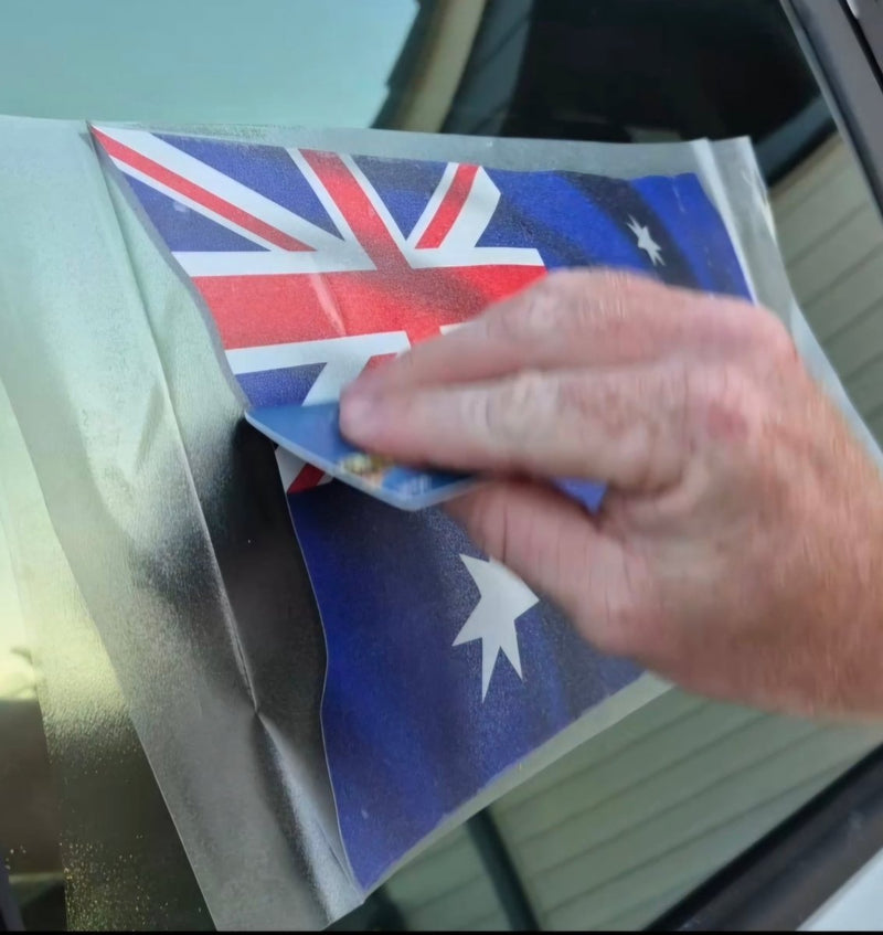 Hand applying an Australian flag decal to a car window.