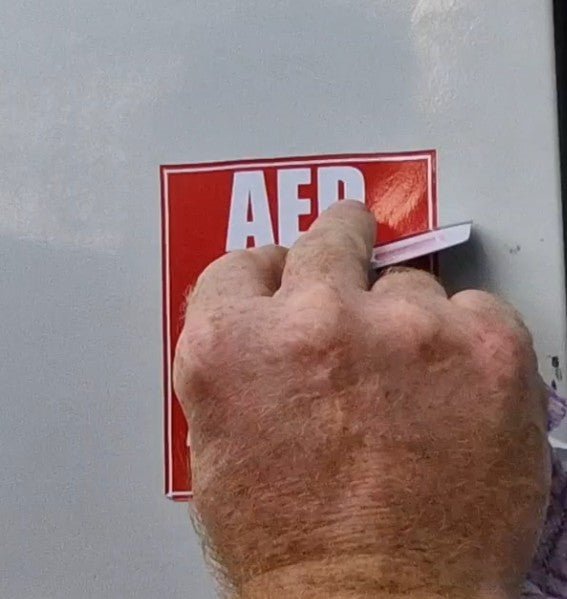 Hand applying a red 'AED' sticker on a surface
