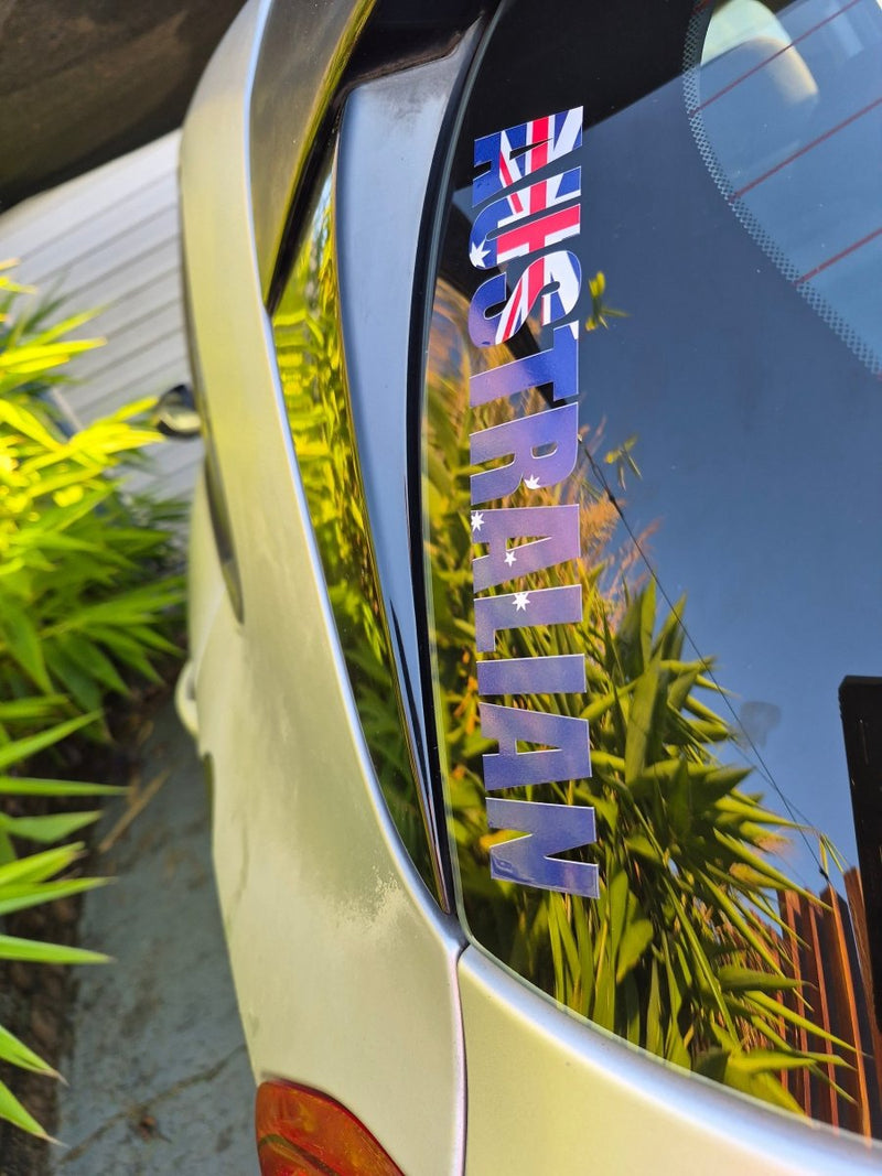 Car window with 'AUSTRALIAN' decal featuring Australia flag, reflecting greenery.