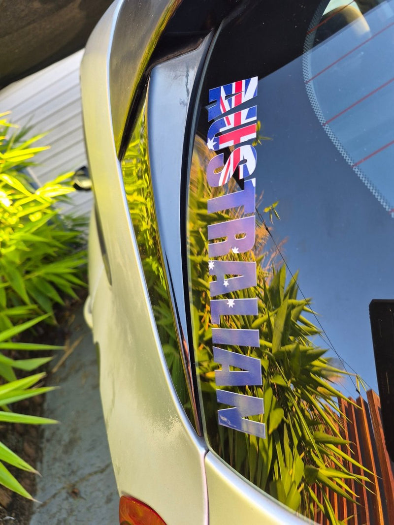 Reflective surface with 'AUSTRALIAN' text and a flag, with plants and building in the background.