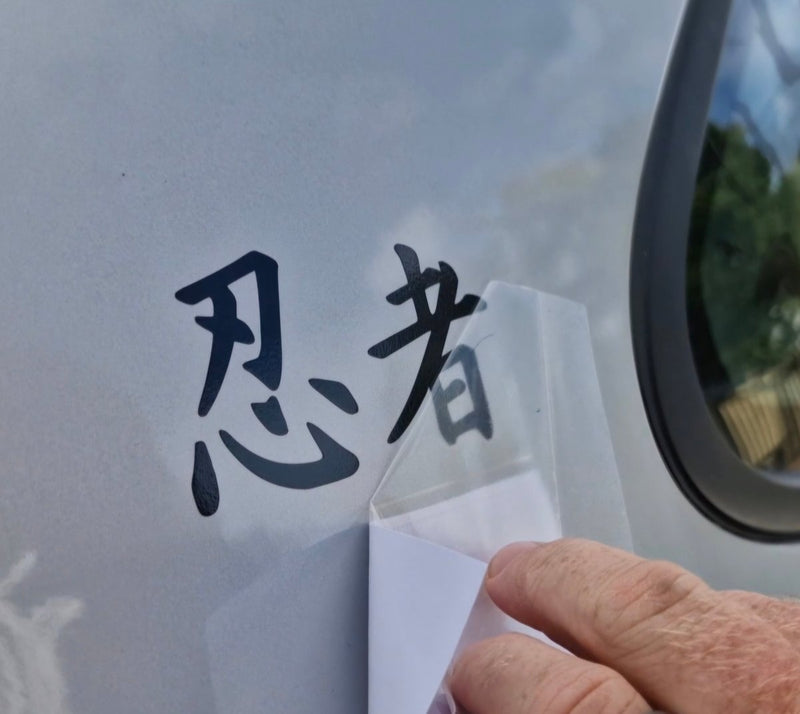 Hand applying a transparent decal with black text on a vehicle window.