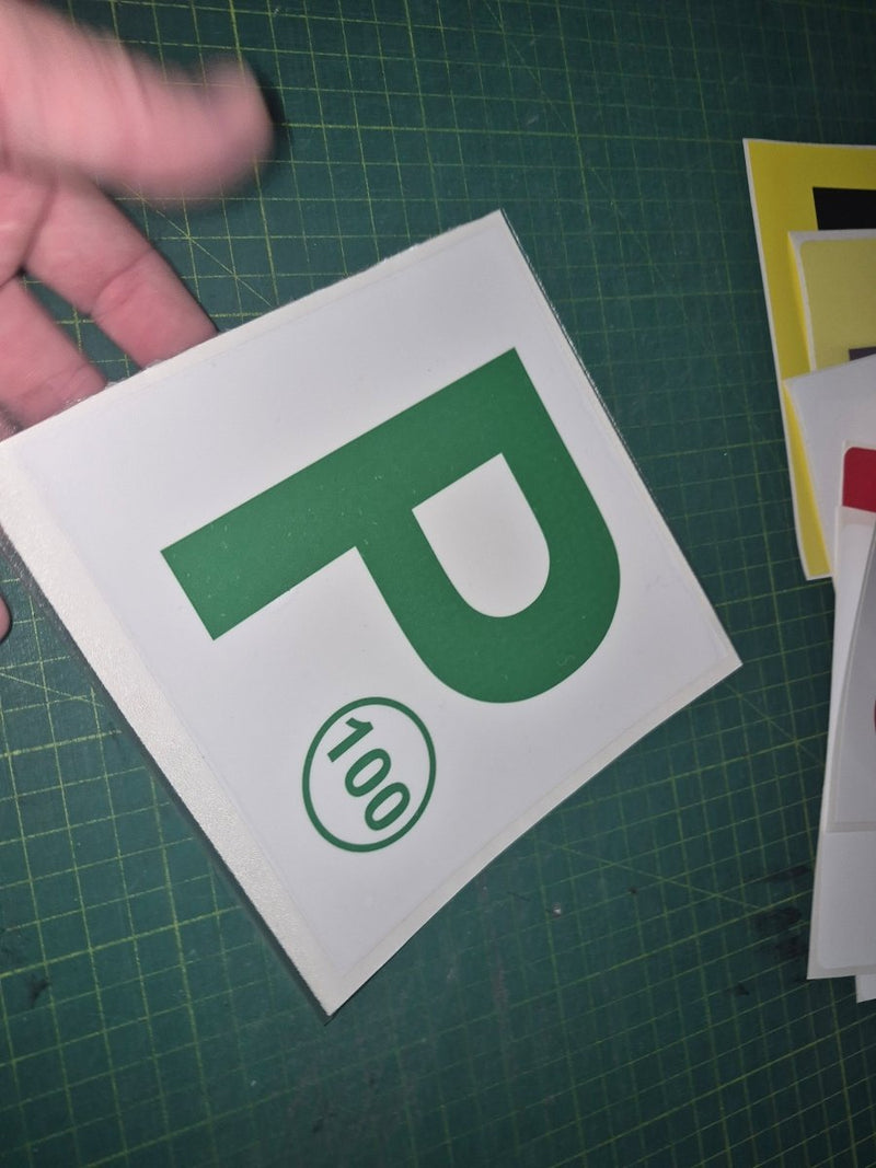 Green 'P' with a number on a white card held over a green cutting mat.