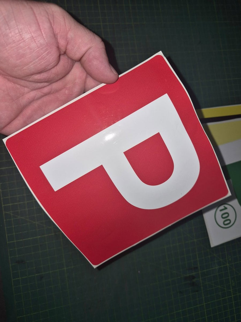 Red square sign with a white 'P' held by a hand on a dark surface.