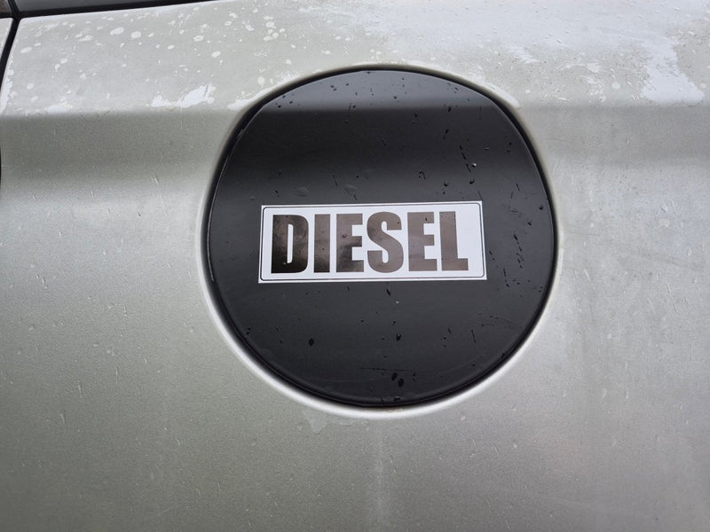 A close-up of a silver car's fuel door featuring a circular black badge with the word 'DIESEL' in white letters.