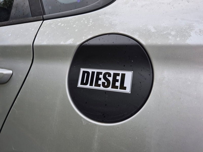 A close-up of a silver car door featuring a black circular fuel door cover with a white and black DIESEL label.