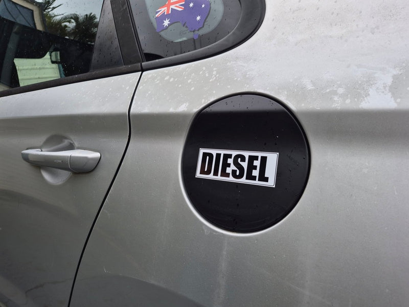 A close-up of the side of a silver car showing a black circular fuel door badge with the word 'DIESEL' in white text. A small Australian flag sticker is visible on the rear window.