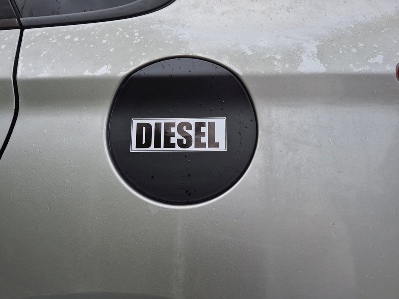 A close-up of a silver car's fuel door featuring a circular black badge with the word 'DIESEL' in white capital letters.