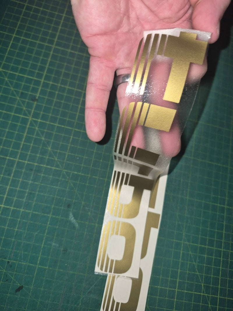 Gold and white decal held over a green cutting mat