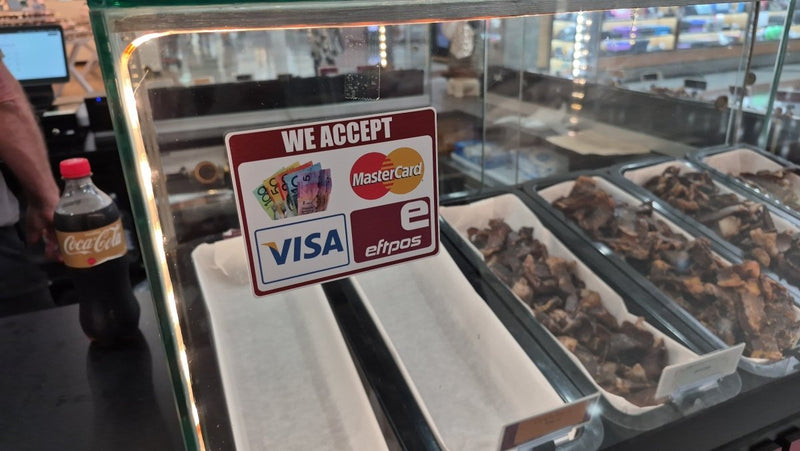 Glass counter with food displays and a sign accepting multiple payment methods.