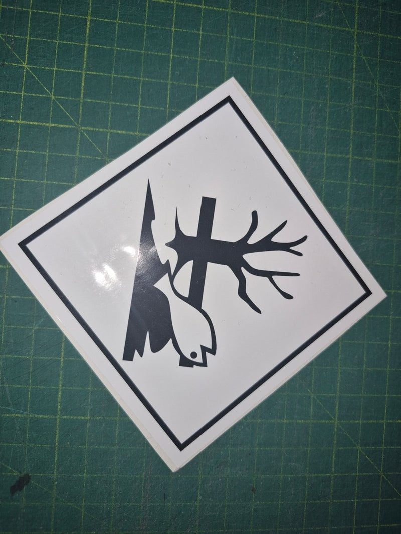 Sticker with a black silhouette of a tree, bird, and lightning bolt on a white background, placed on a green cutting mat.