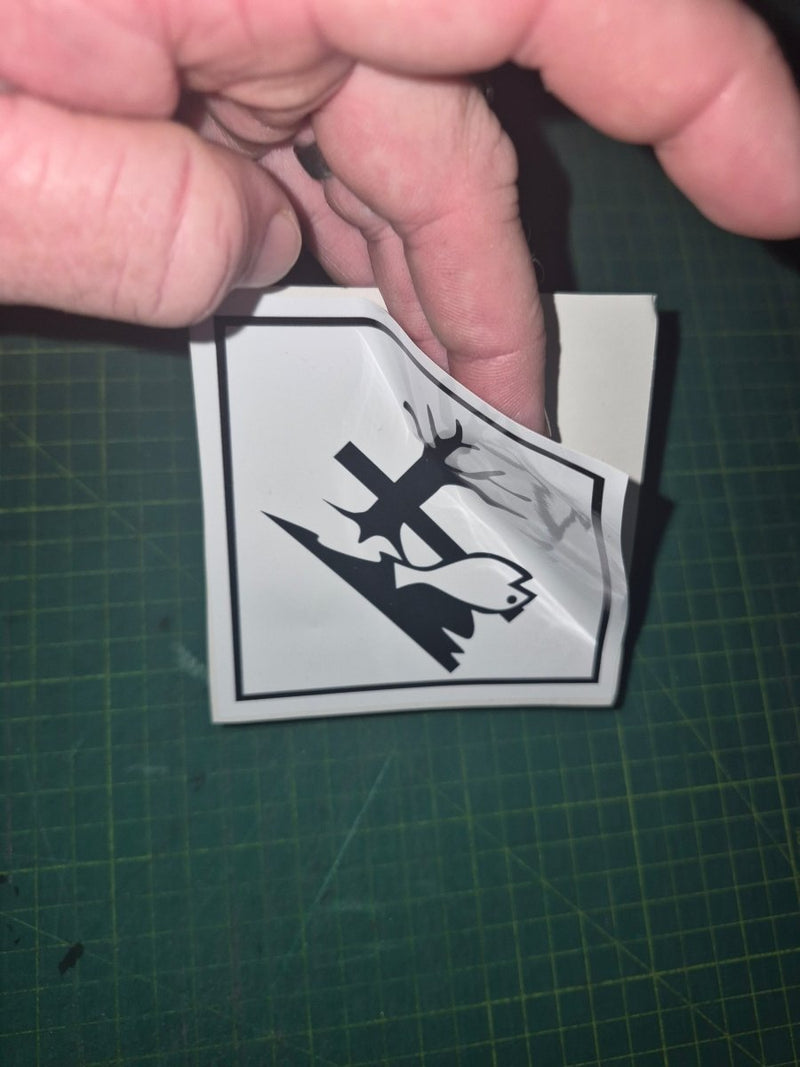 Hand holding a small black and white sticker with a design on a green cutting mat.