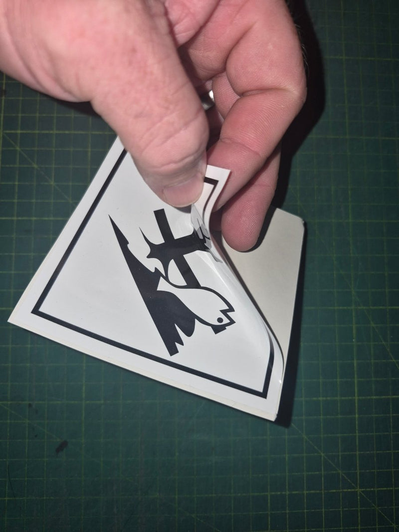 Hand holding a warning label with a bird and exclamation mark on a green cutting mat.
