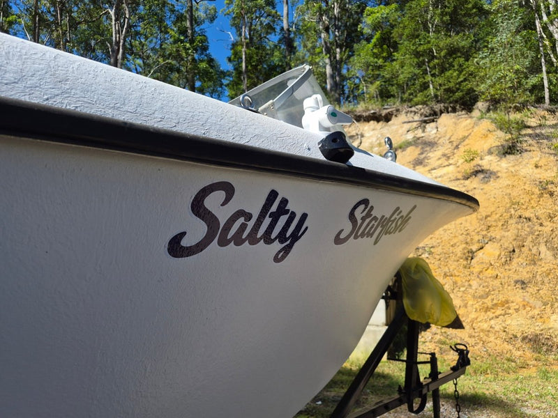 White boat with custom made decal of  'Salty Starfish' branding on a grassy area with trees in the background, Australian made