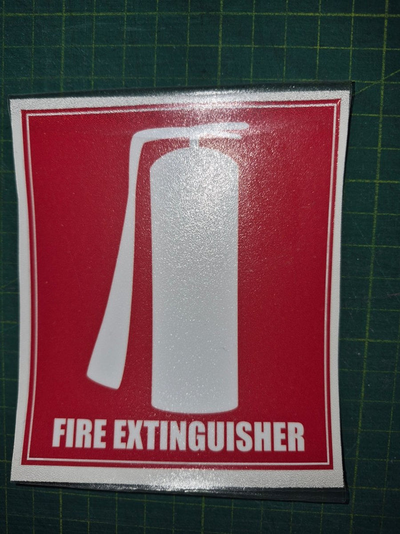 Fire extinguisher sign on a red background with white text and symbol, placed on a green cutting mat.