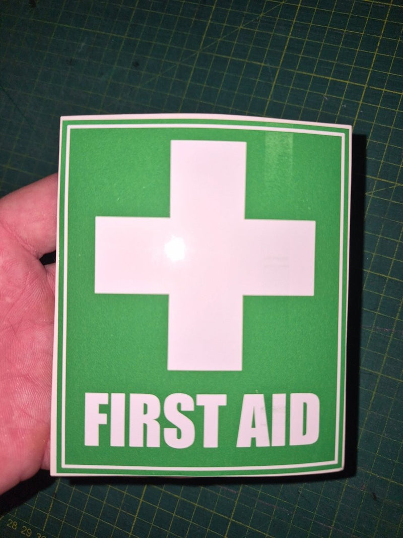 First aid sign with a cross on green paper held by a hand on a grid background