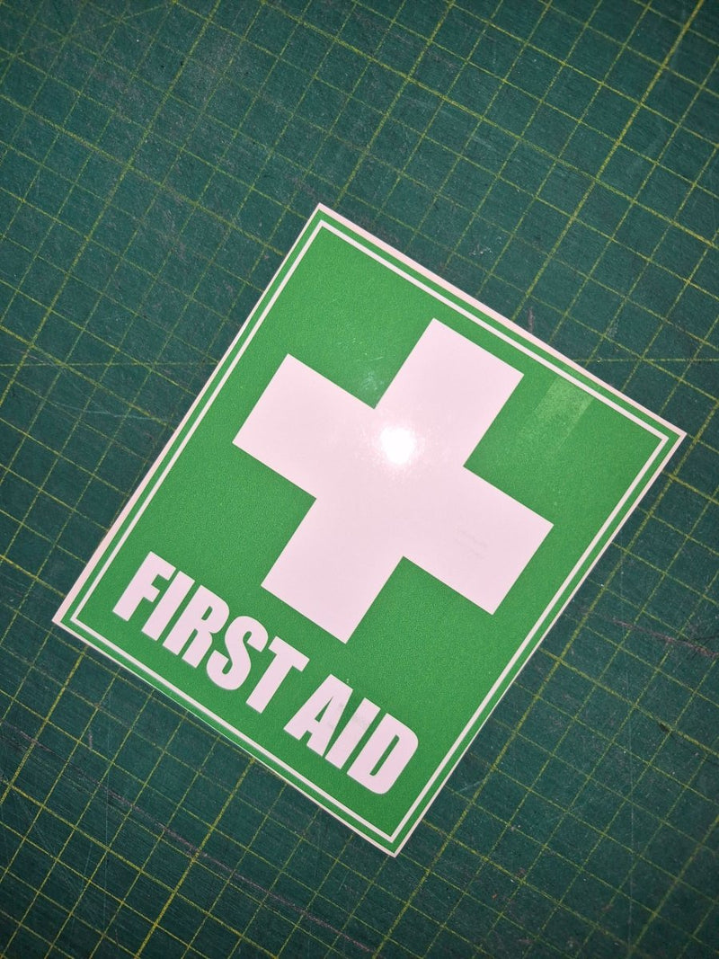First aid sign with a white cross on a green background, placed on a grid surface.