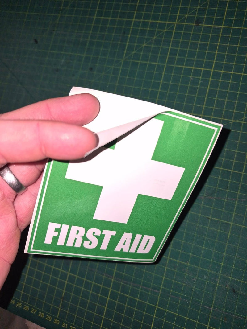Hand holding a green and white first aid sign on a grid background