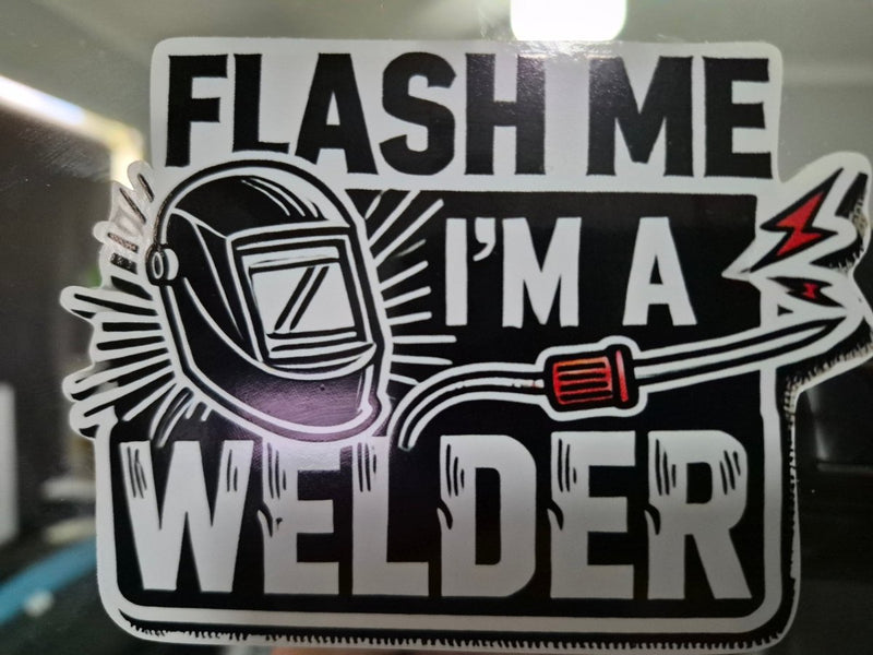Sticker with a welding helmet and text 'Flash me I'm a welder' on a reflective surface.