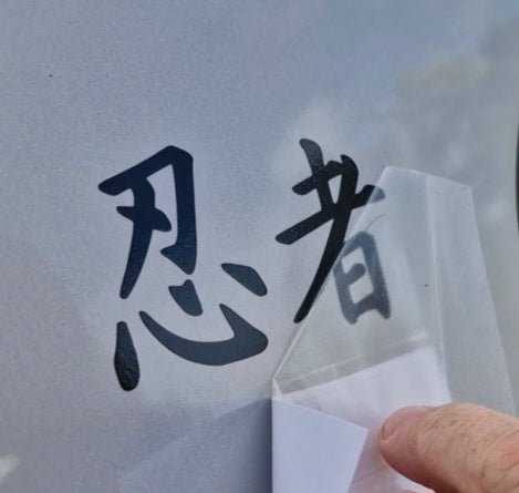 Decal of Japanese font saying ninja characters on a textured surface with a clear plastic sheet.