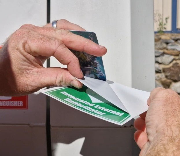 Person holding a green and white label with text, against a neutral background.