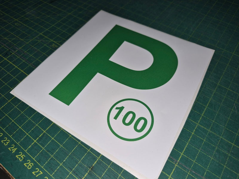 Green 'P' and number 100 sign on a white background, placed on a green cutting mat.
