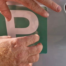 Load image into Gallery viewer, Hand placing a green license plate with a white 'P' on a vehicle.
