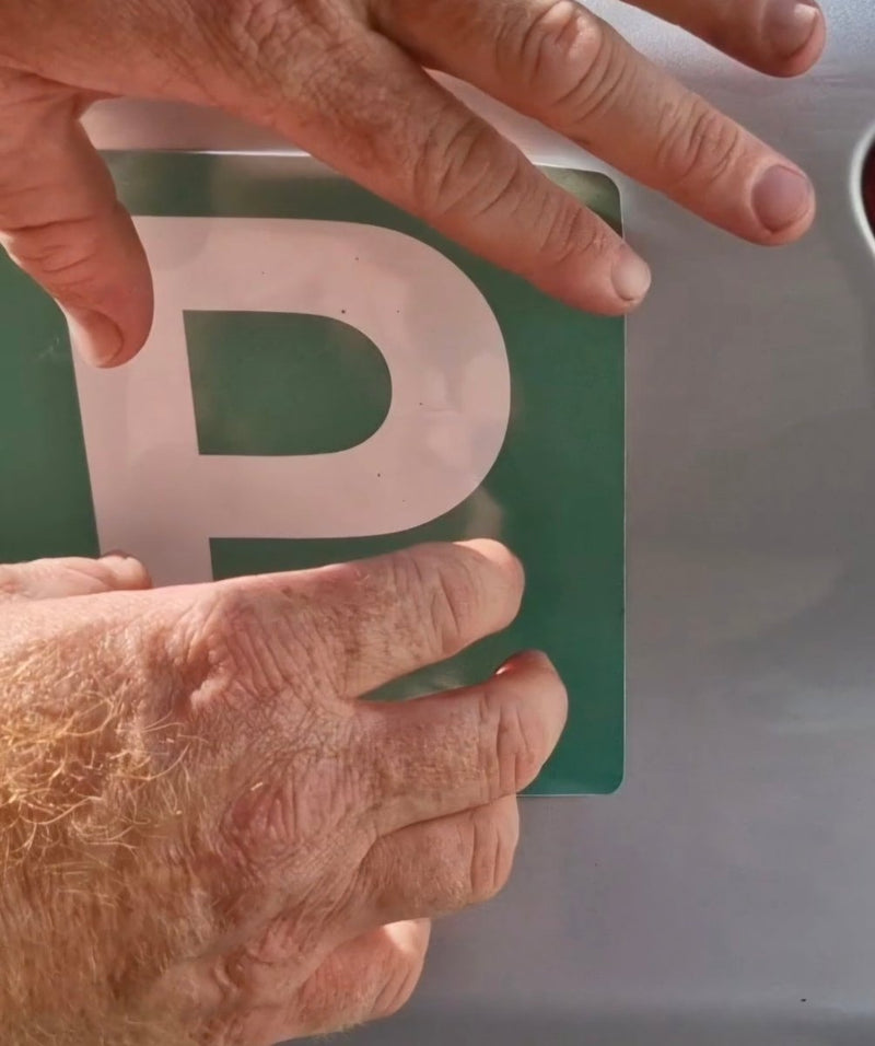 Hand placing a green license plate with a white 'P' on a vehicle.