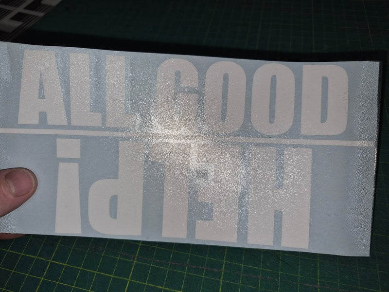Decal with 'ALL GOOD HERE!' text held over a cutting mat