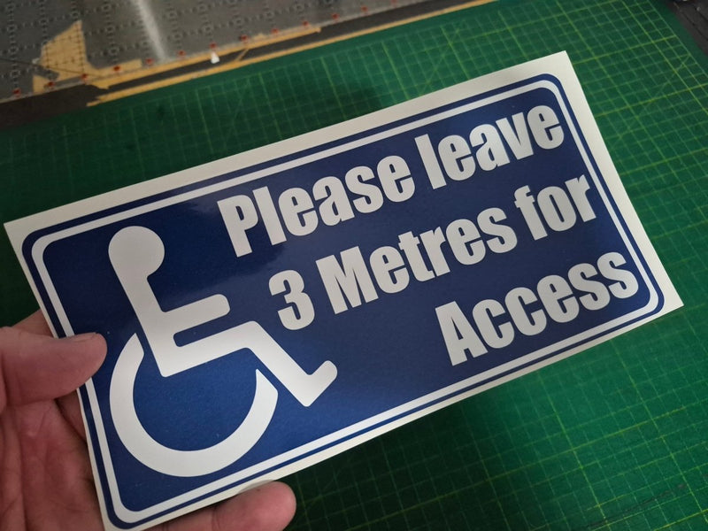 Handheld sign with wheelchair icon and text 'Please leave 3 Metres for Access' on a green cutting mat.