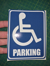 Load image into Gallery viewer, Handicap parking sign held by a hand on a green grid background
