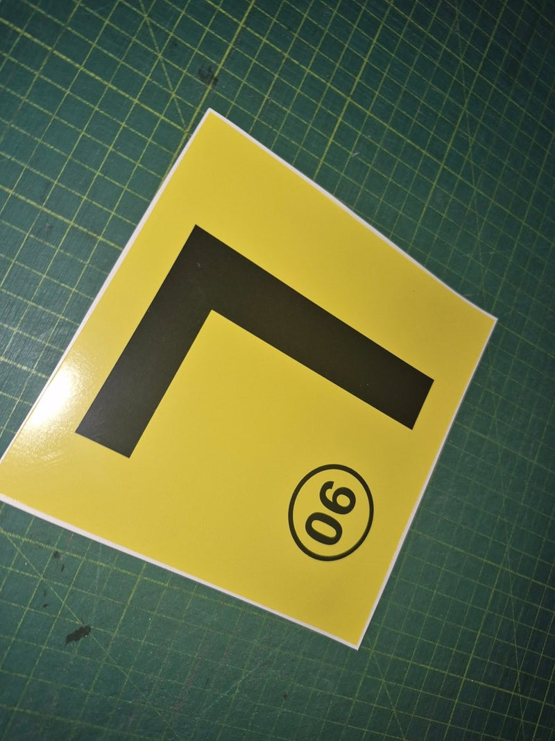 Yellow square with a black 'L' and a black circle with number 90 on a green grid background