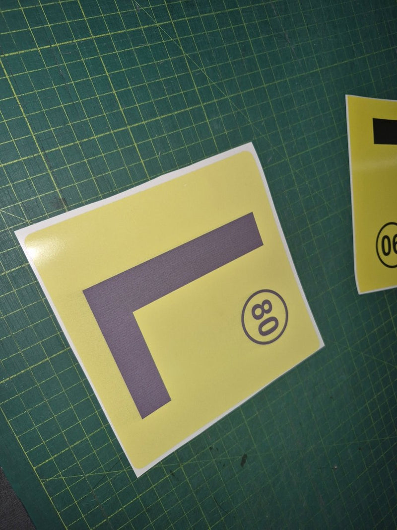 Yellow square with a purple 'L' and black number '80' on a green grid background