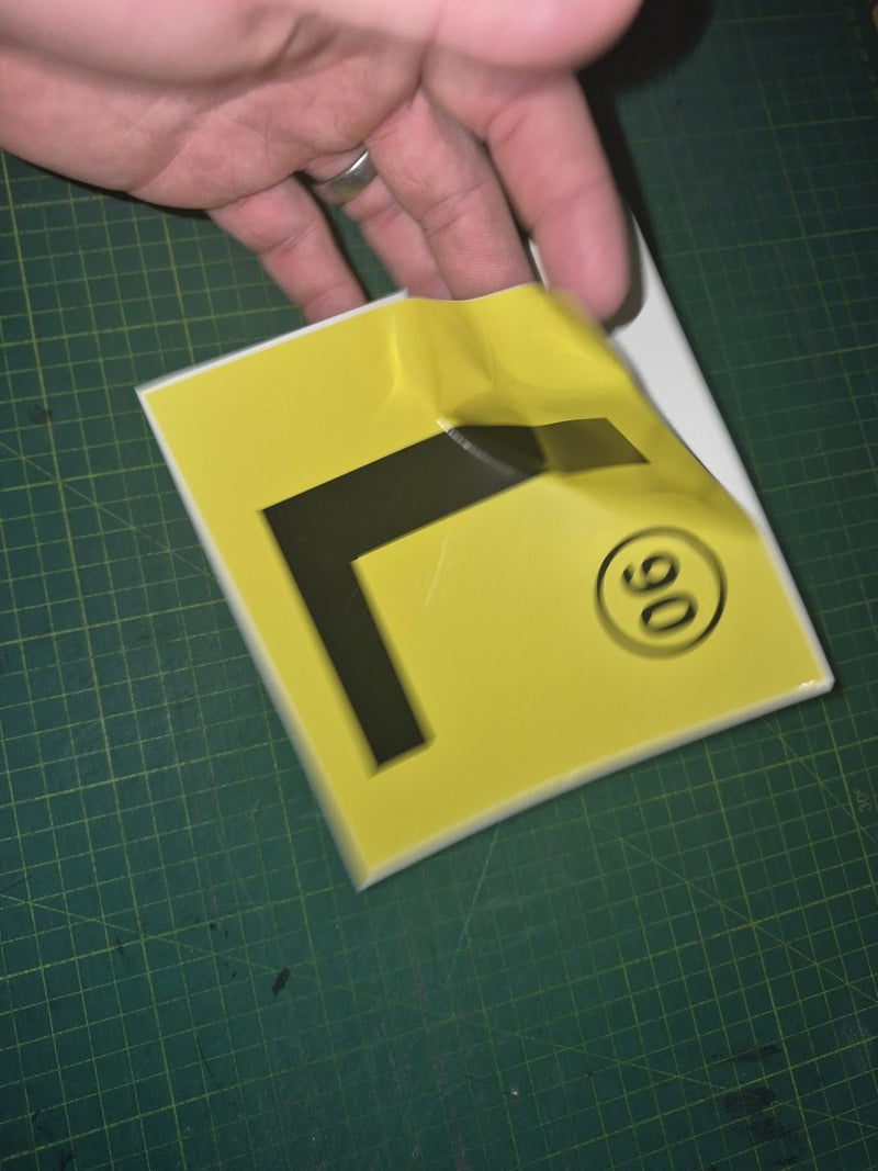 Yellow square with a black 'L' shape and number 90 on a green cutting mat.