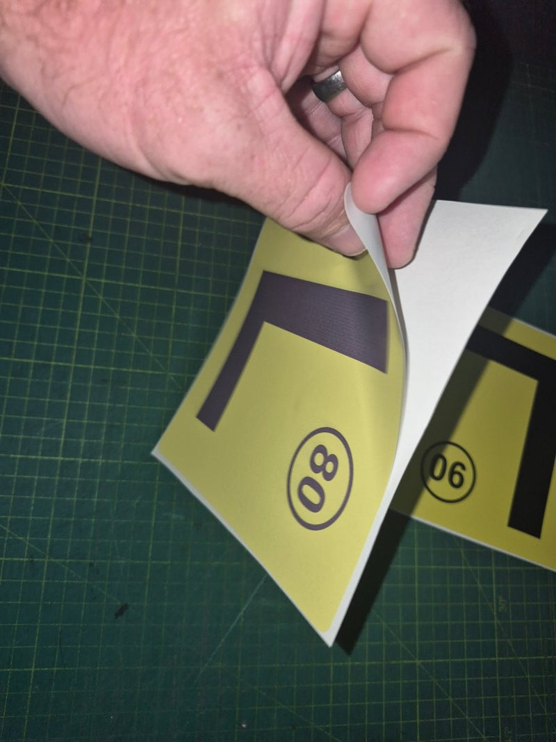 Hand holding a yellow traffic sign with black lettering on a green cutting mat.