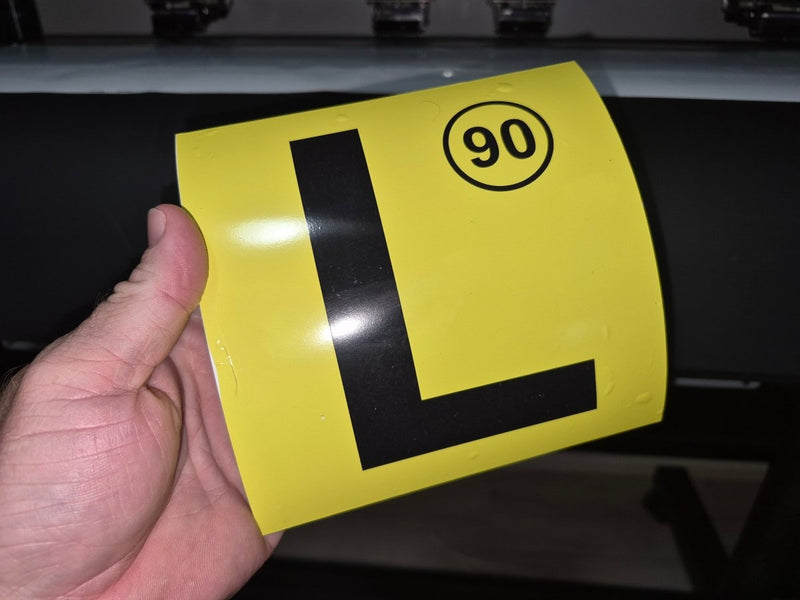Yellow license plate with black 'L' and number 90 held by a hand against a dark background
