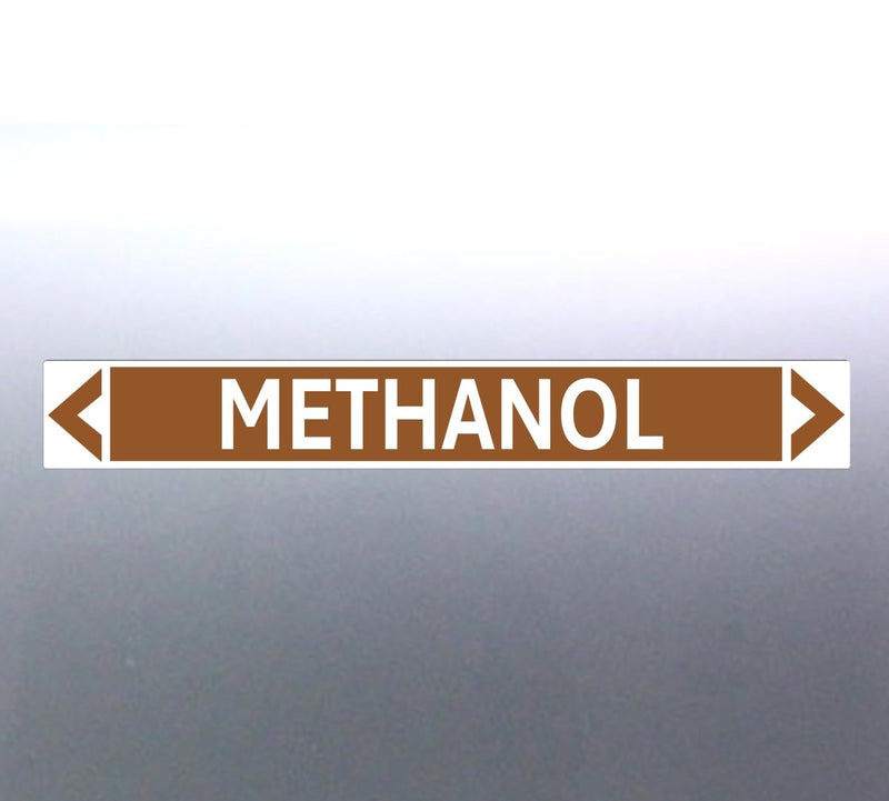A pipe marker label with the word 'METHANOL' in bold black lettering on a golden tan background, with a white border and green directional arrows pointing in both directions.