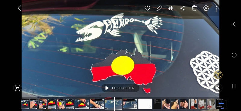 Car window with decorative stickers, including a fish skeleton, Aboriginal flag, and geometric design.