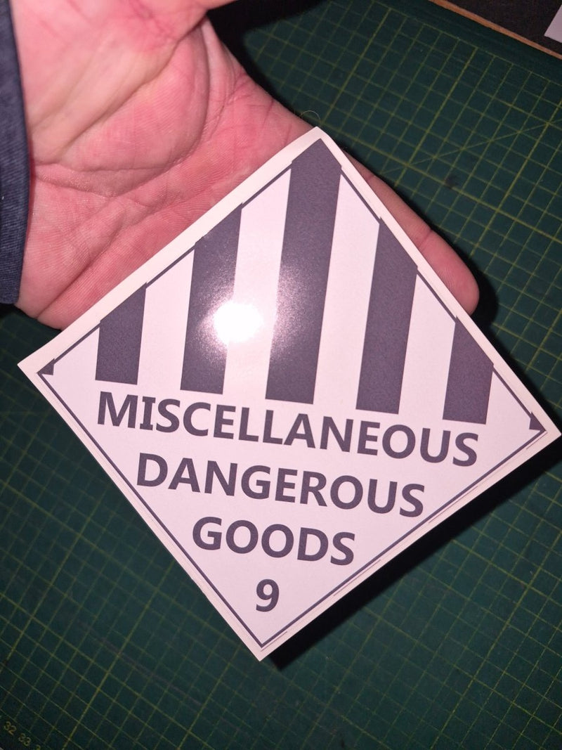 Sticker with 'Miscellaneous Dangerous Goods' text held over a green cutting mat.